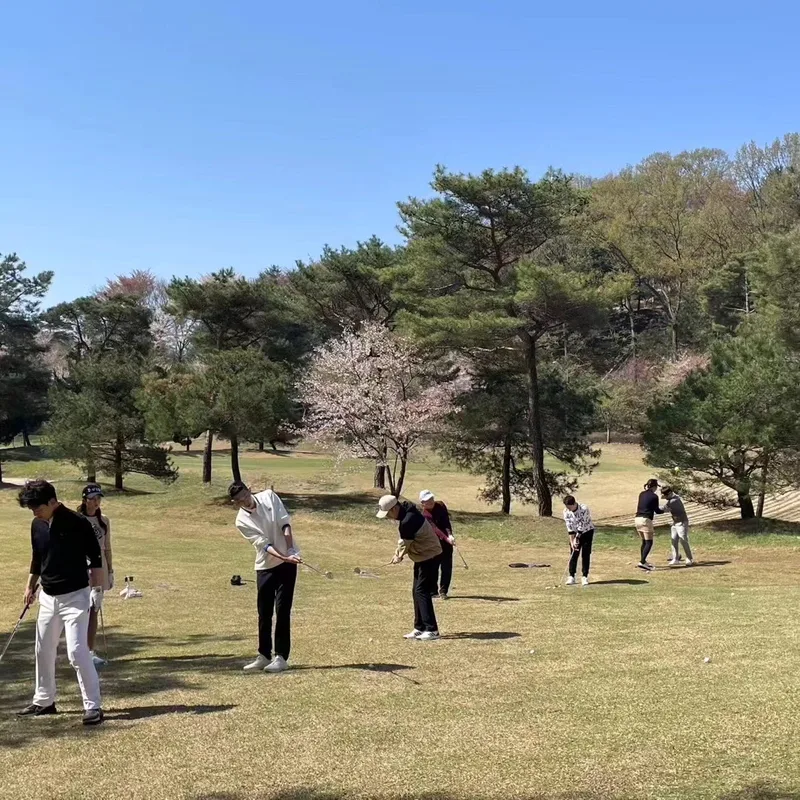 야외 잔디 연습장에서 참가자 여러 명이 나란히 서서 어프로치를 연습하는 모습
